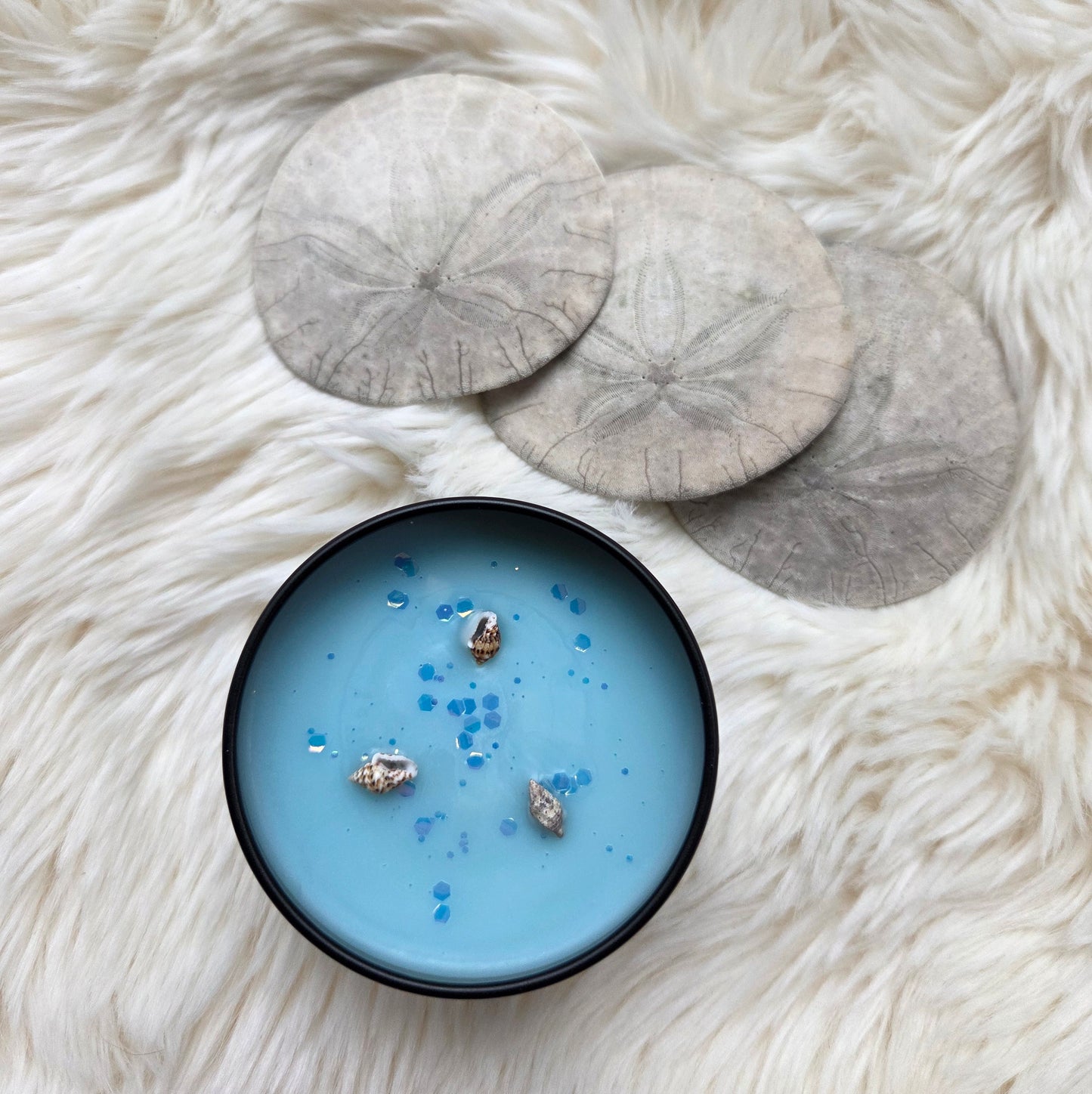 Blue candle with seashells inside on a white fur surface