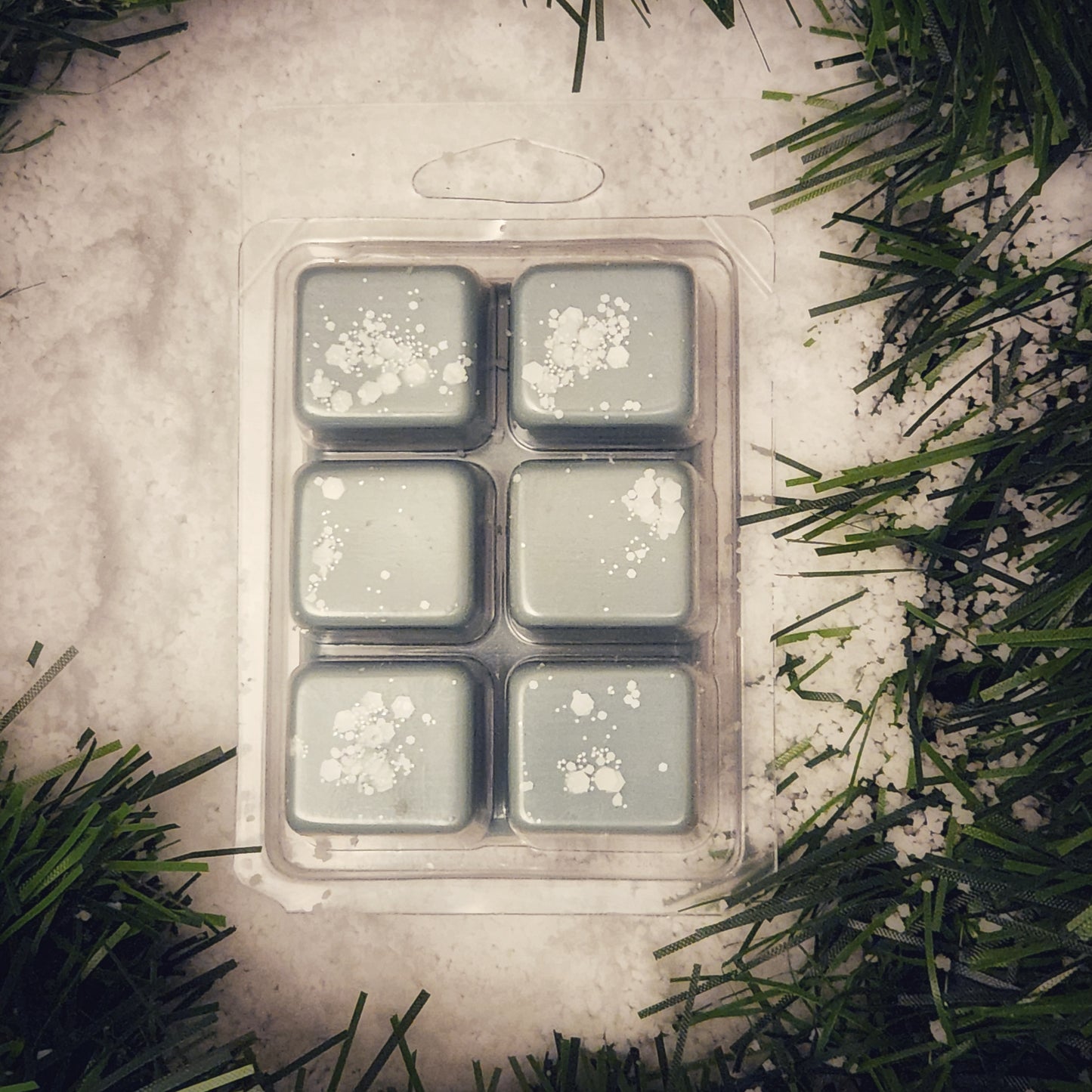 Pack of six green wax melts with white decorative elements on a textured surface with greenery.