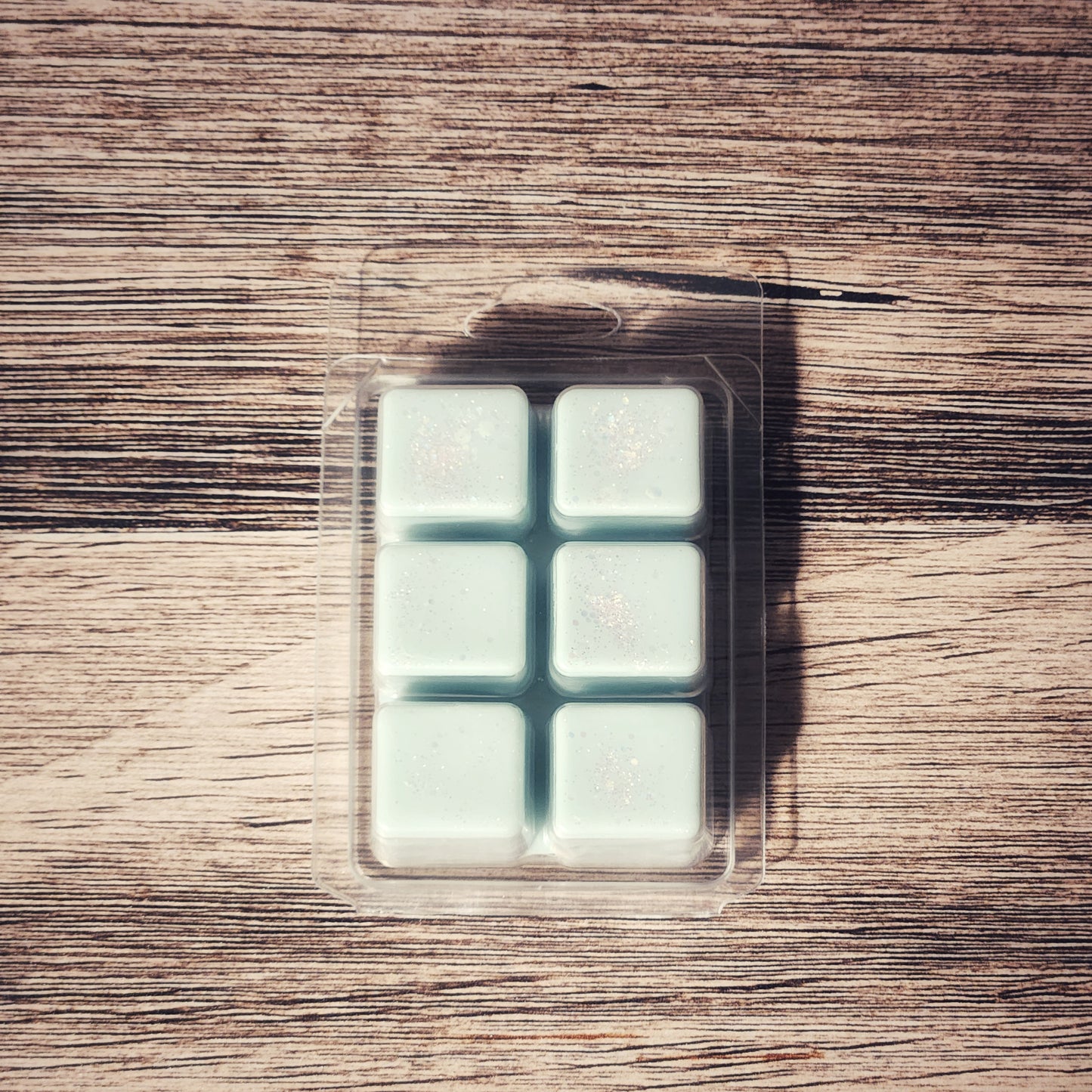Clear plastic packaging with six light blue wax melts on a wooden surface