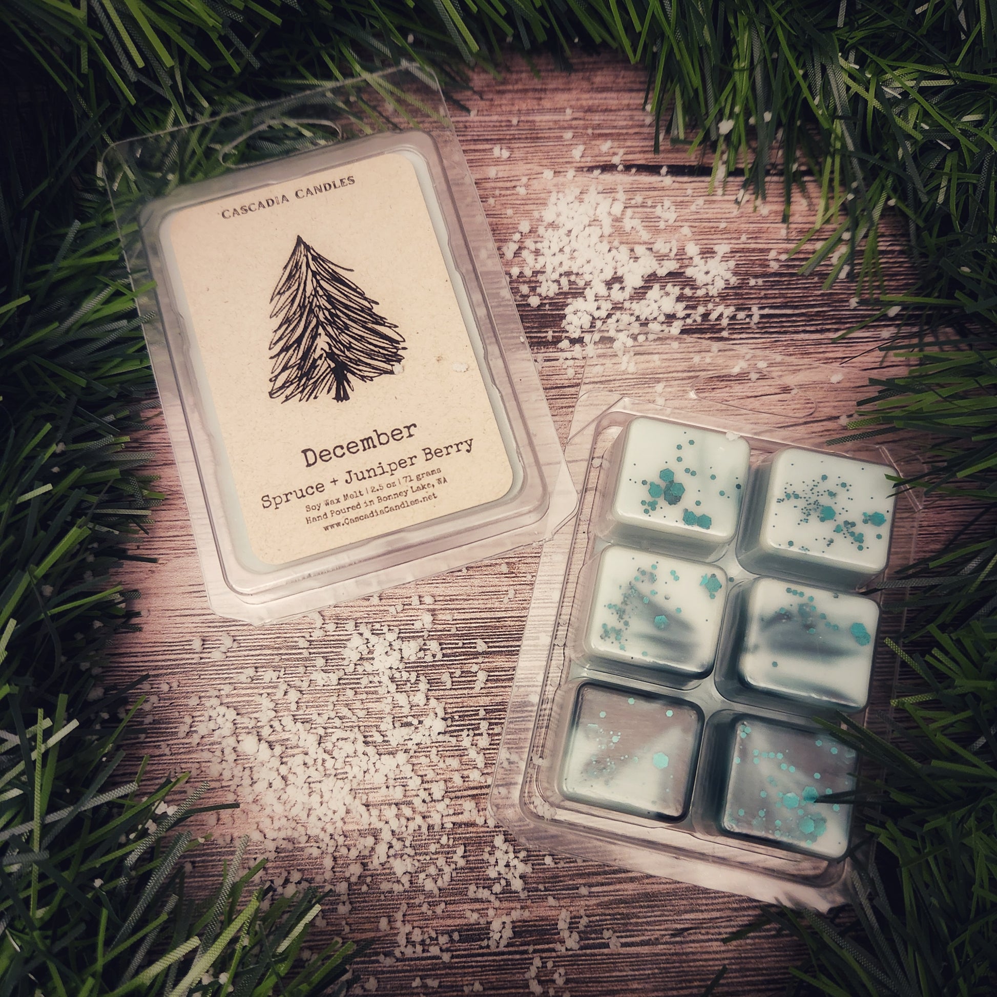 Packaged wax melts with a tree design on a wooden surface surrounded by greenery