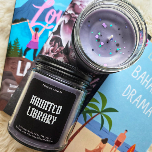 Candle jar labeled 'Haunted Library' with a purple candle on top, placed on some books.