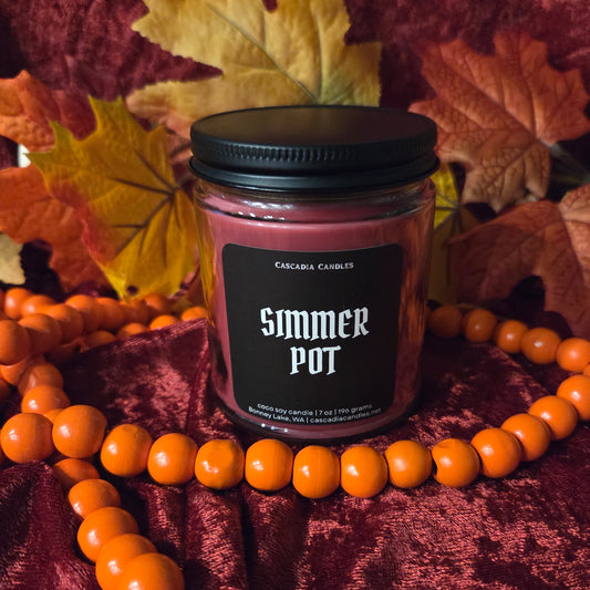 Simmer Pot candle in front of a red velour background with orange garland and fall leaf decor.