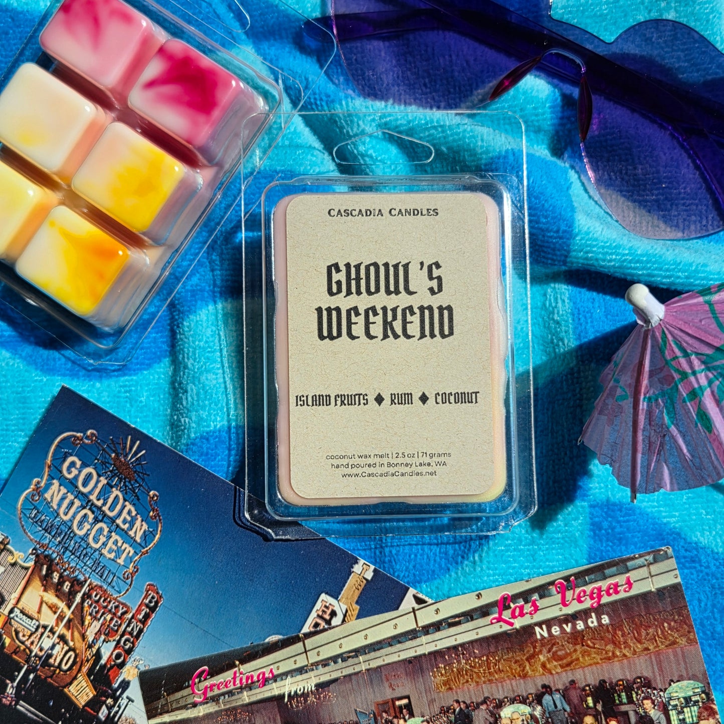 Cascadia Candles 'Ghoul's Weekend' wax melt package on a blue surface with sunglasses and Las Vegas-themed cards.