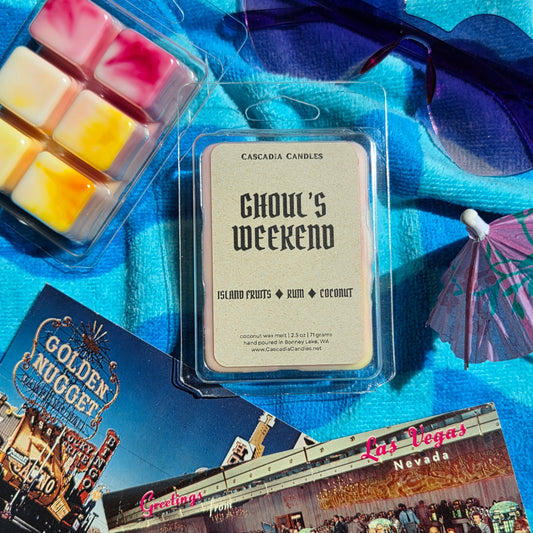 Cascadia Candles 'Ghoul's Weekend' wax melt package on a blue surface with sunglasses and Las Vegas-themed cards.