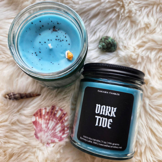 Candle jar labeled 'Dark Tide' on a fluffy white surface.