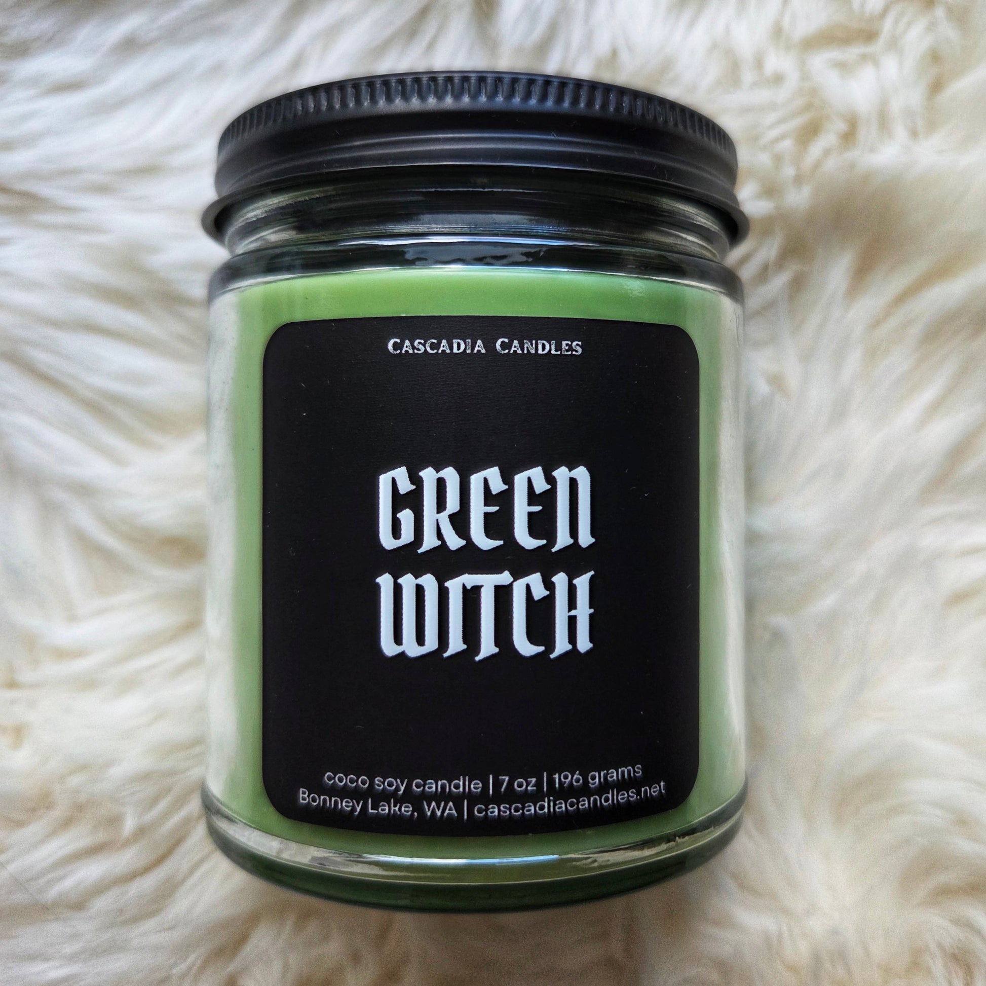 Green candle labeled 'Green Witch' by Cascadia Candles on a white fluffy surface