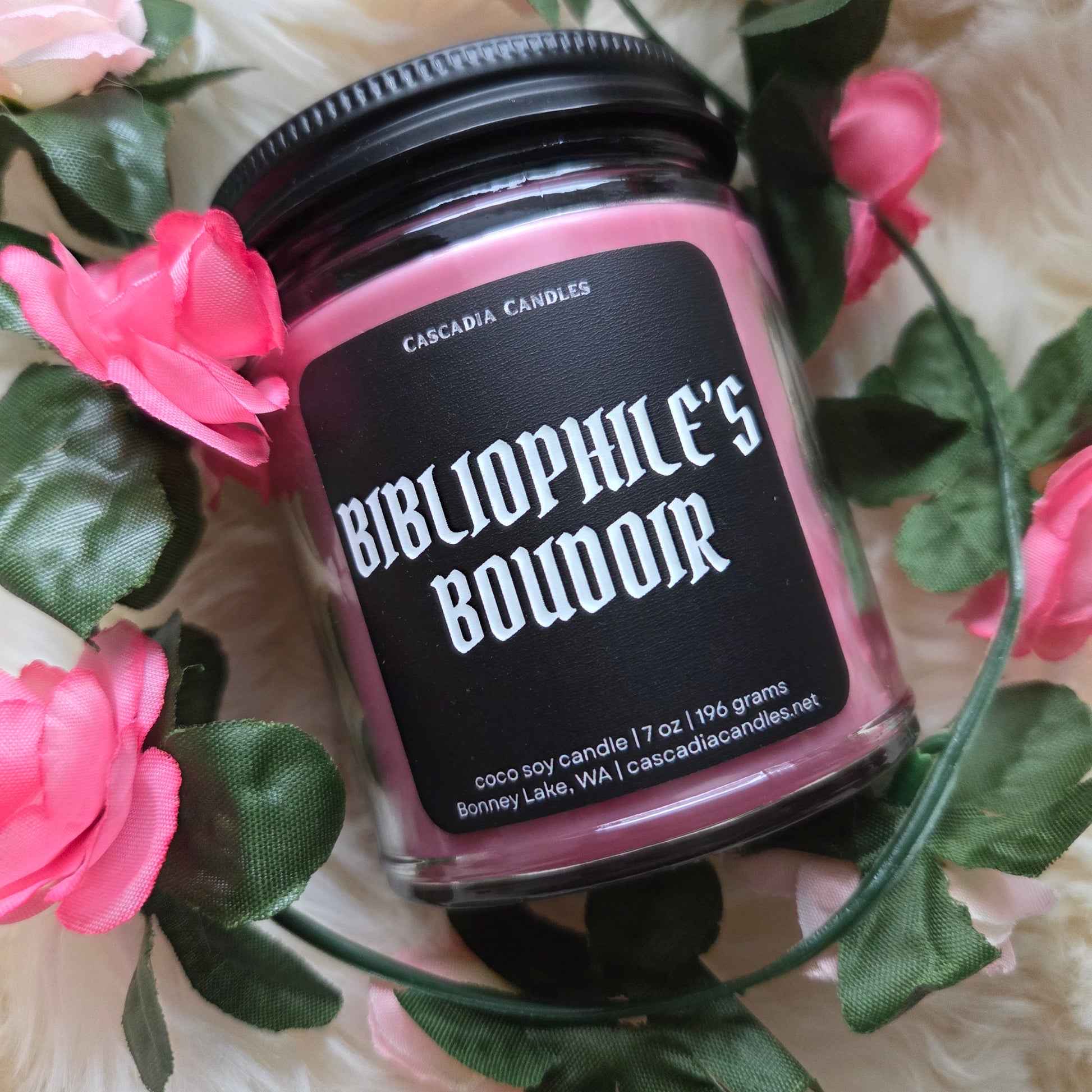 Candle jar labeled 'Bibliophile's Bouddoir' surrounded by pink flowers and green leaves.