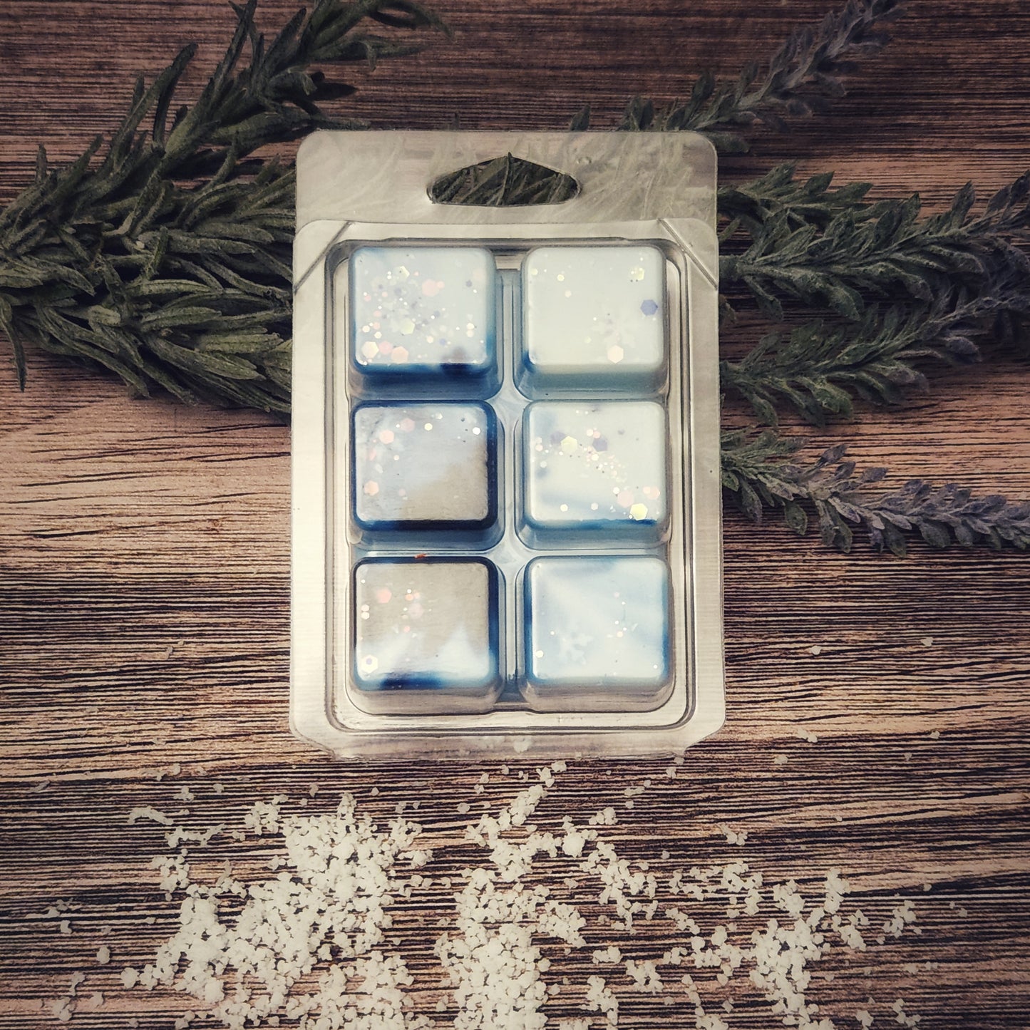 Plastic wax melt clamshell with six compartments on a wooden surface with greenery and snow-like material.