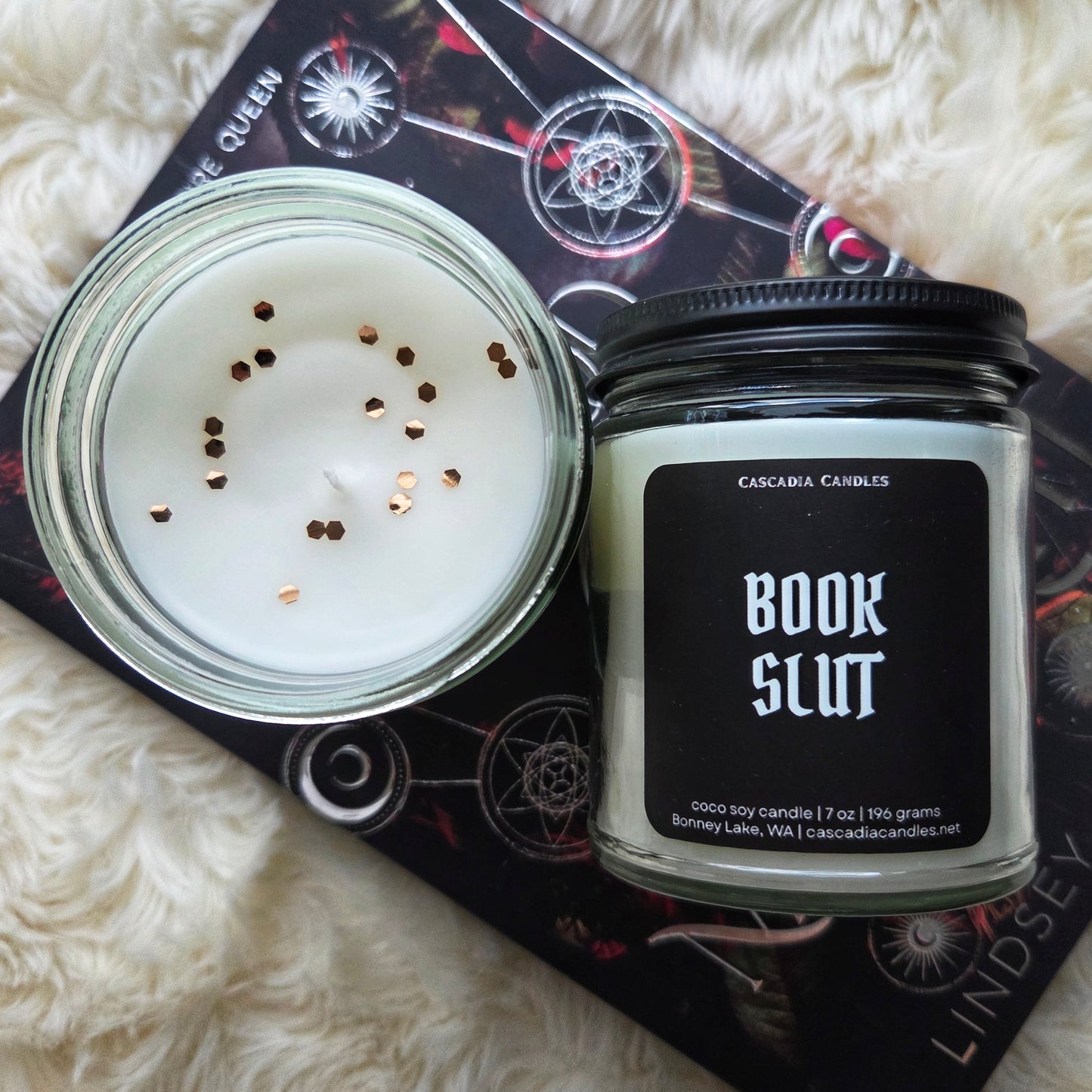 Candle in a jar with 'Book Slut' label on a fluffy white surface