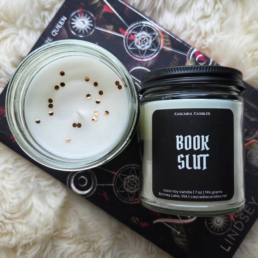 Candle in a jar with 'Book Slut' label on a fluffy white surface