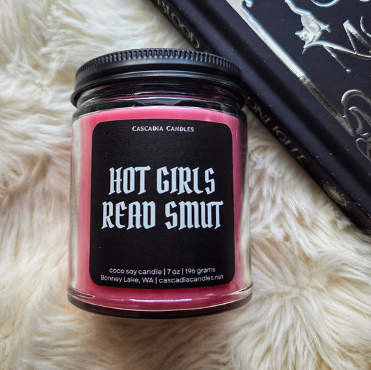 Candle jar with 'Hot Girls Read Smut' text on a fluffy white surface
