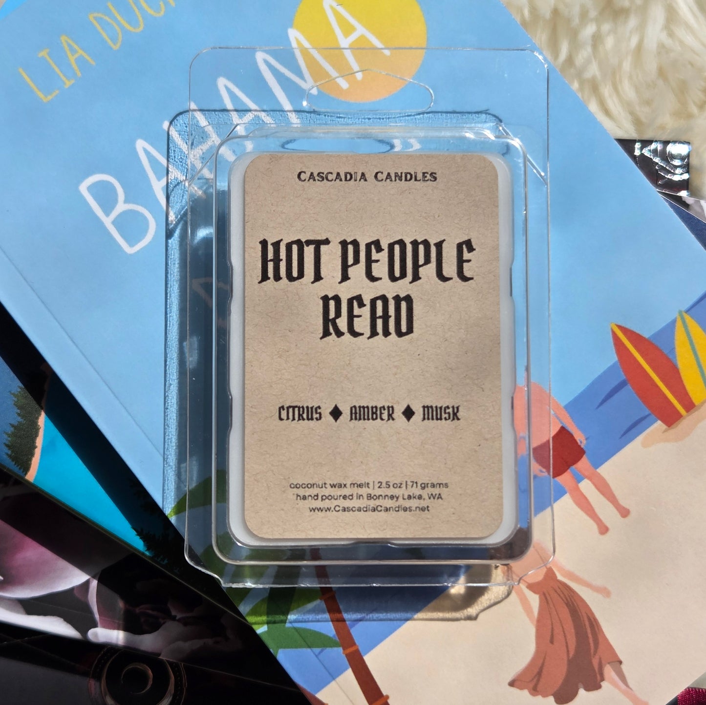 A single wax melt package from Cascadia Candles reading 'Hot People Read' with 'Citrus Amber Musk' scent, placed on top of colorful books.