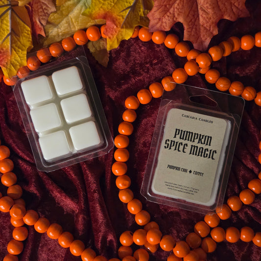 Two packaged wax melts from Cascadia Candles, 'Pumpkin Spice Magic' in a 6-count clamshell and a single 6-count melt in clear packaging, styled on a dark red velvet fabric with orange beads and autumn leaves.