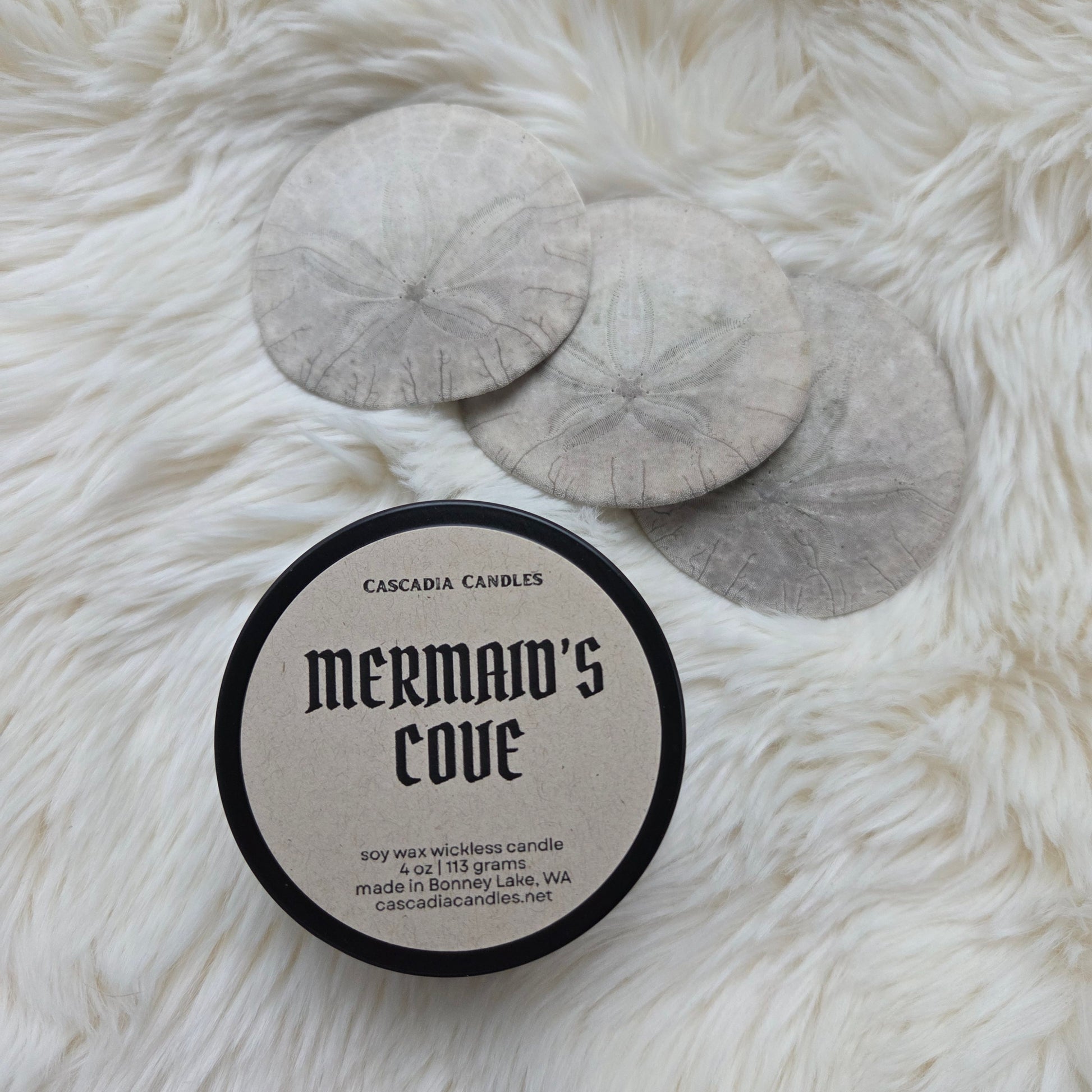 Candle labeled 'Mermaid's Cove' by Cascadia Candles on a fluffy white surface.