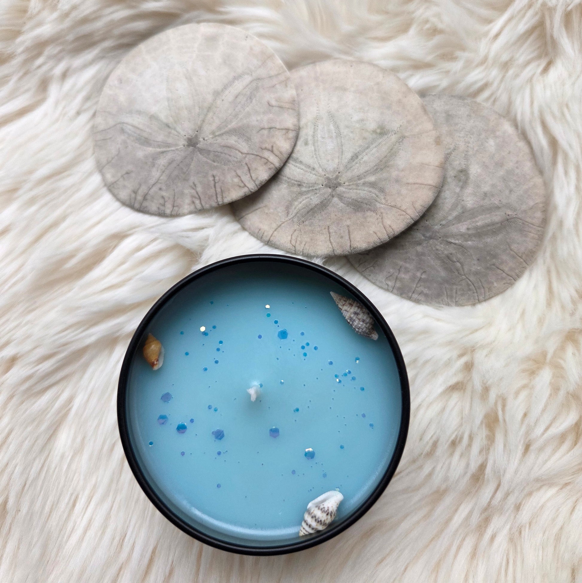 Blue candle with glitter and shells on a white fluffy surface
