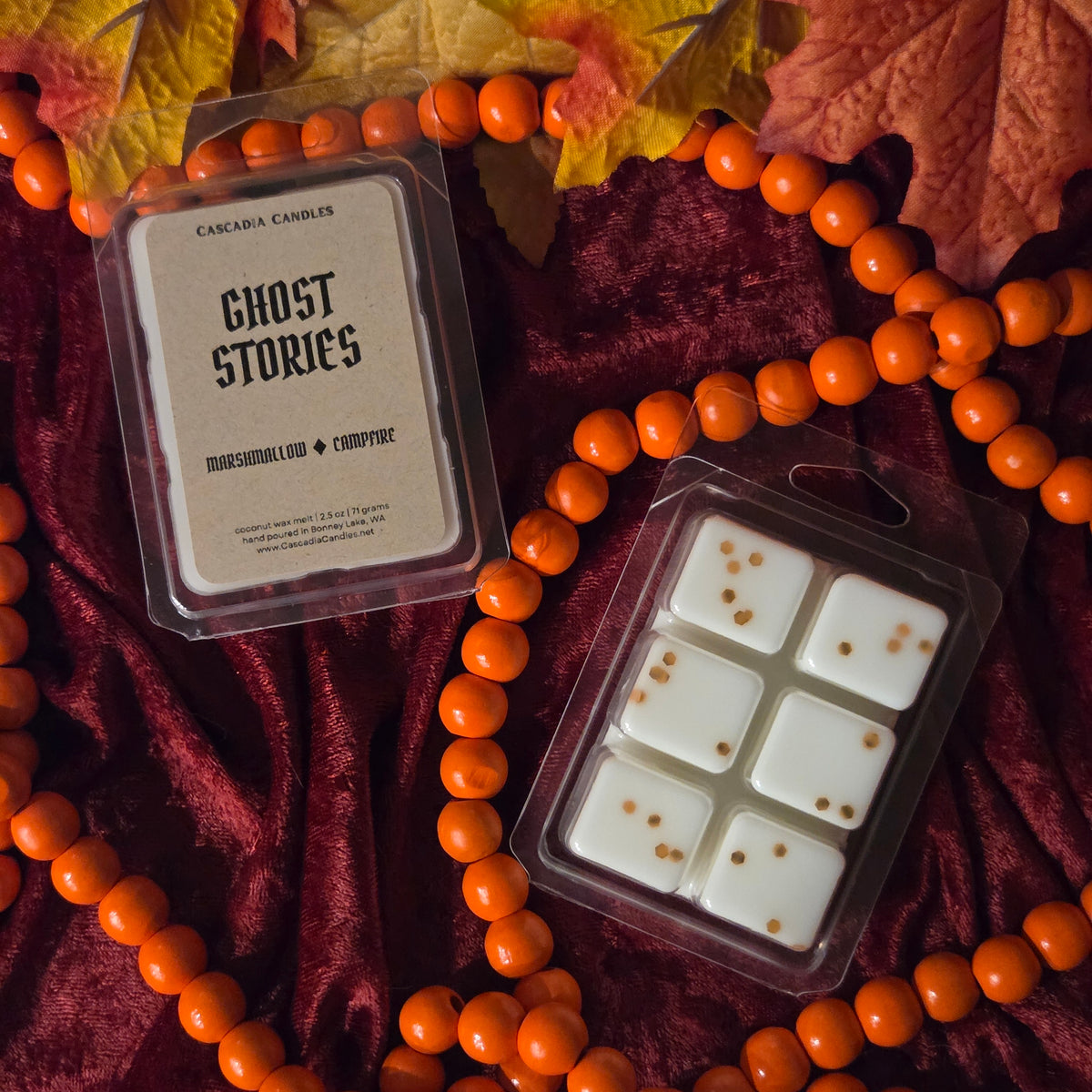 Ghost Stories wax melt made by Cascadia Candles resting on a red velour fabric with orange bead garland and faux leaf decor.