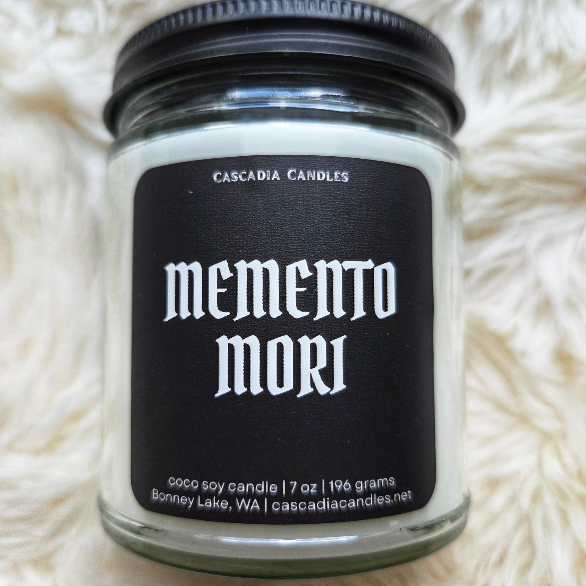 Candle jar labeled 'memento mori' by Cascadia Candles on a white fluffy surface
