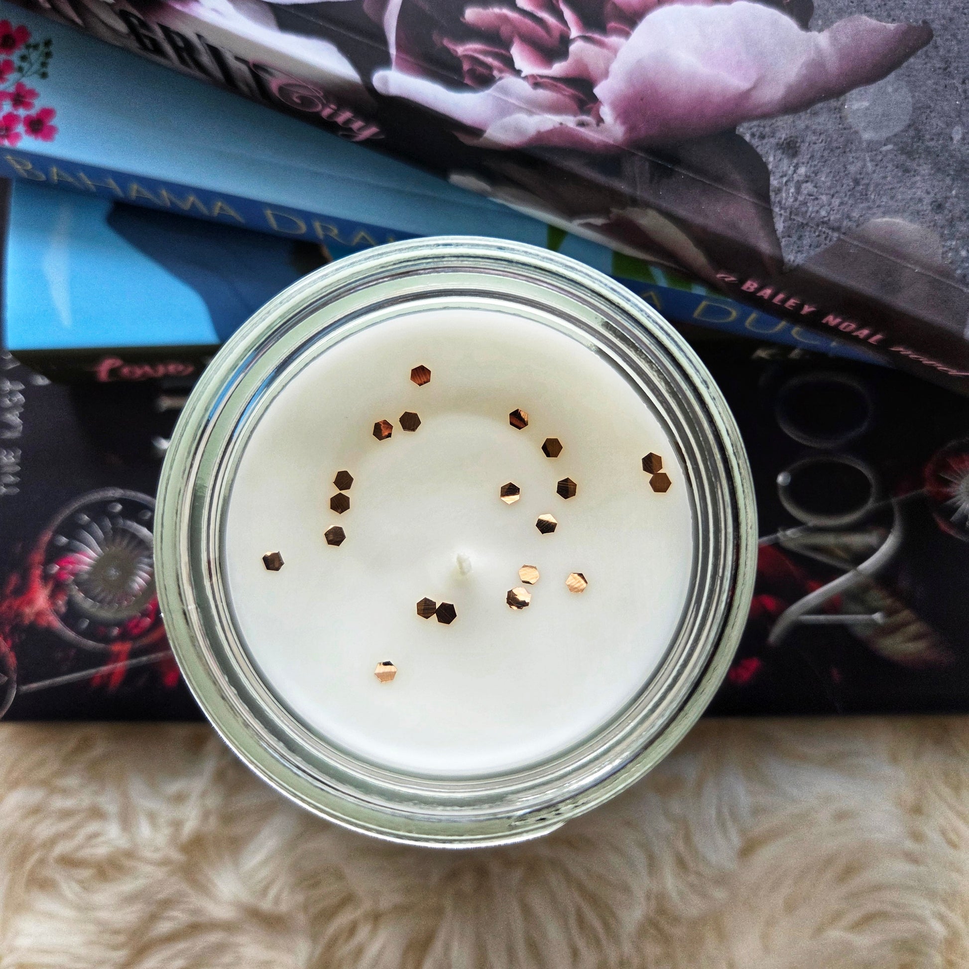 Candle in a glass jar with visible wick on top of books