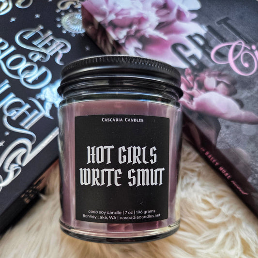 Candle jar with 'Hot Girls Write Smut' text on a textured surface
