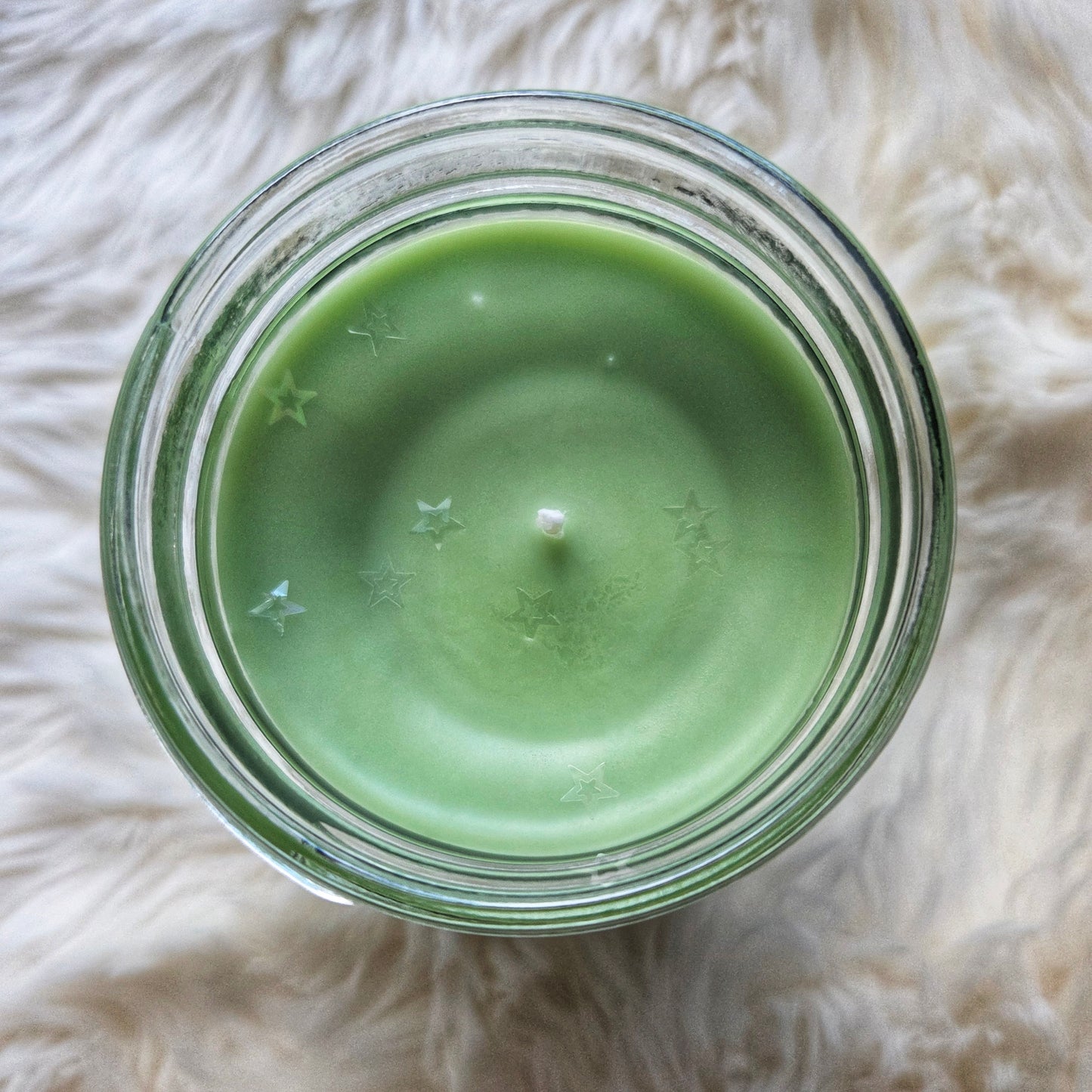 Green candle in a glass jar on a fluffy white surface