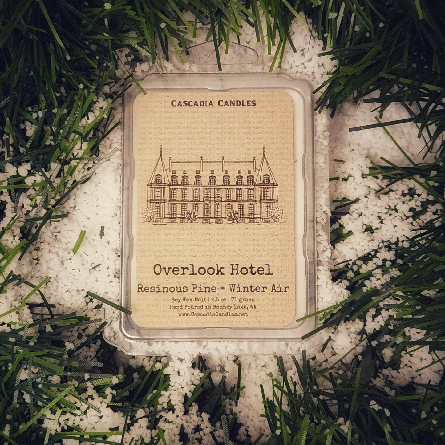 Cascadia Candles Overlook Hotel candle packaging on a snowy background with evergreen branches.