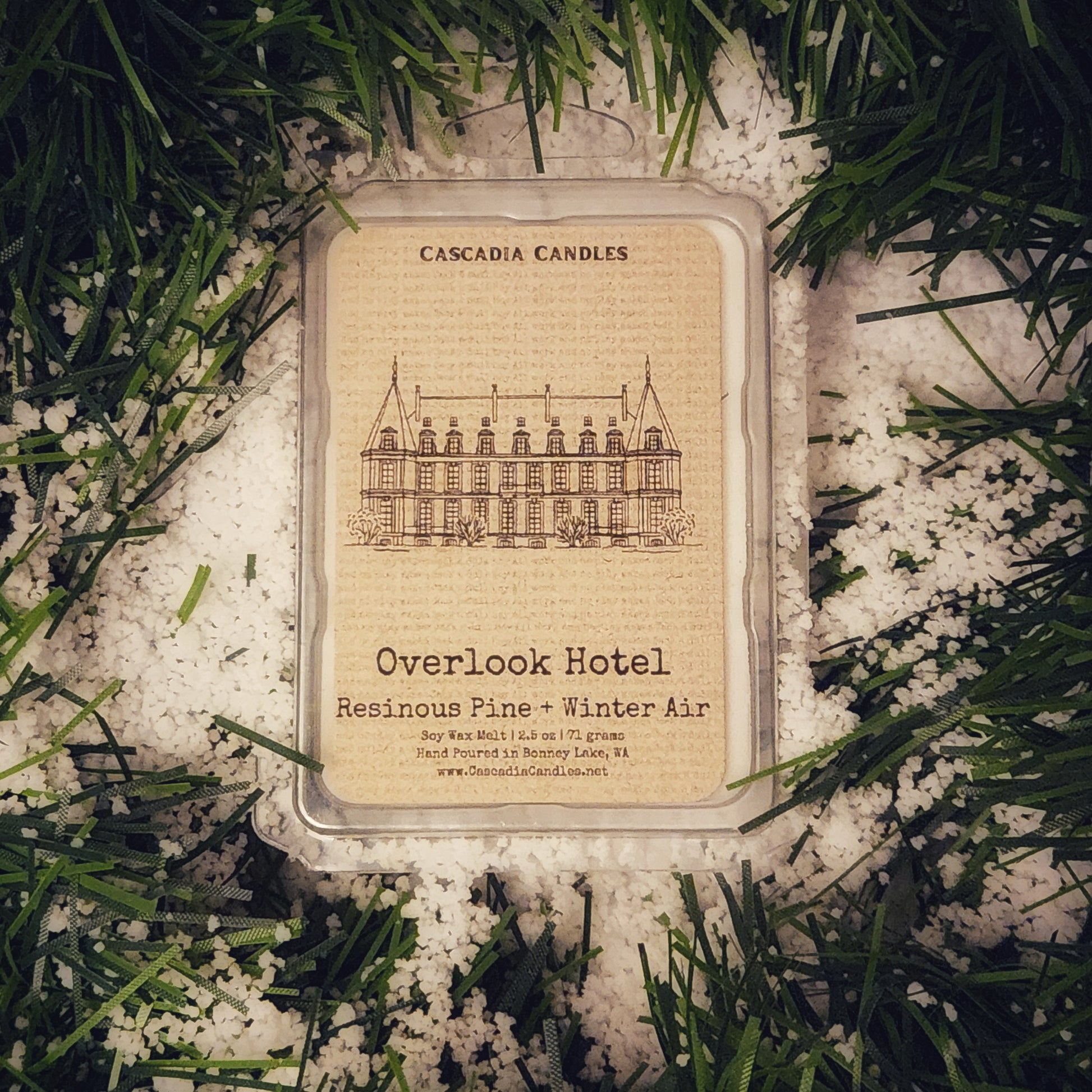 Cascadia Candles Overlook Hotel candle packaging on a snowy background with evergreen branches.