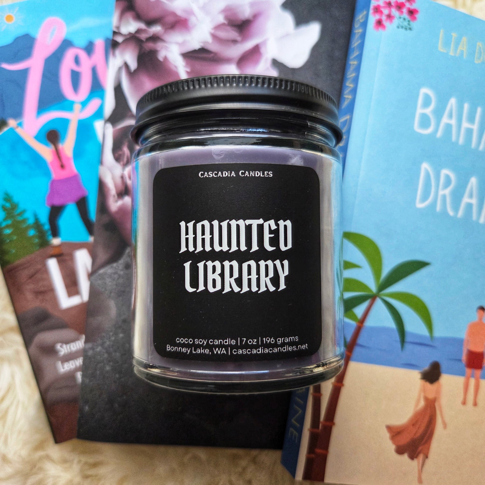 Candle labeled 'Haunted Library' by Cascadia Candles on a surface with books in the background.