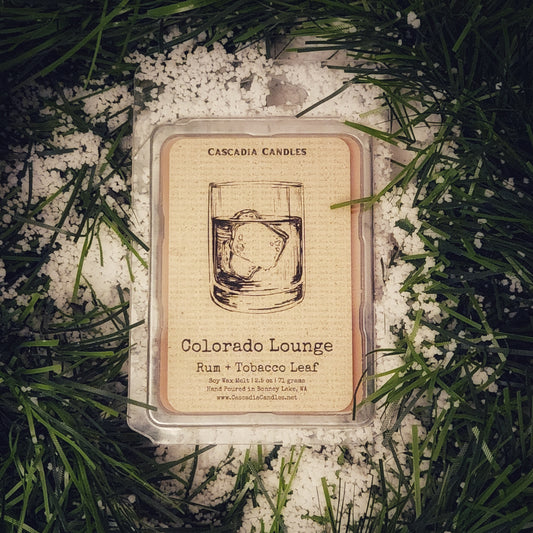 Cascadia Candles Colorado Lounge candle packaging on a snowy background with greenery.