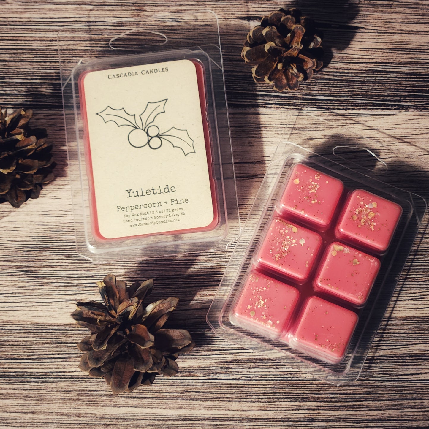 Packaged red wax melts with 'Yuletide' label on a wooden surface with pine cones.
