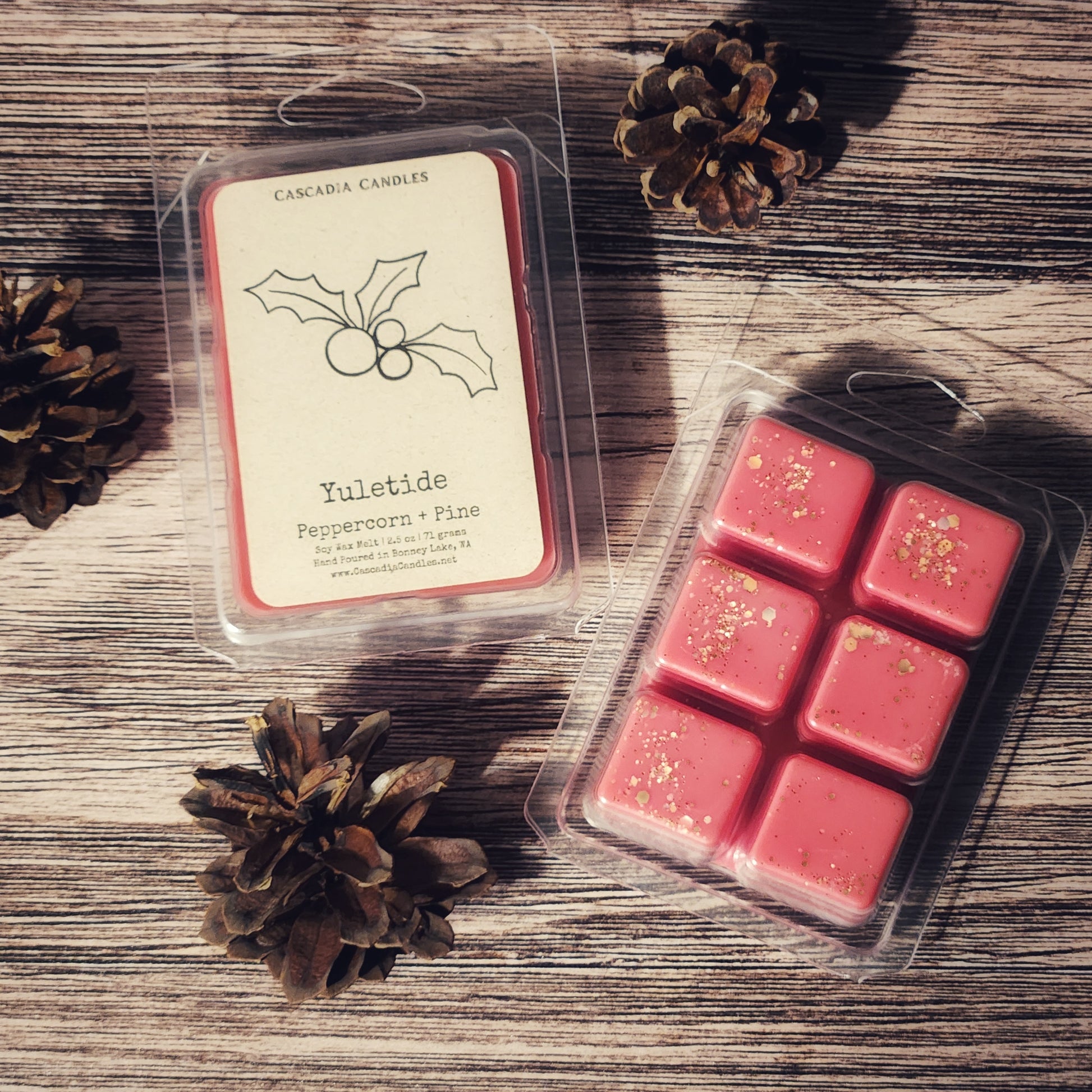 Packaged red wax melts with 'Yuletide' label on a wooden surface with pine cones.