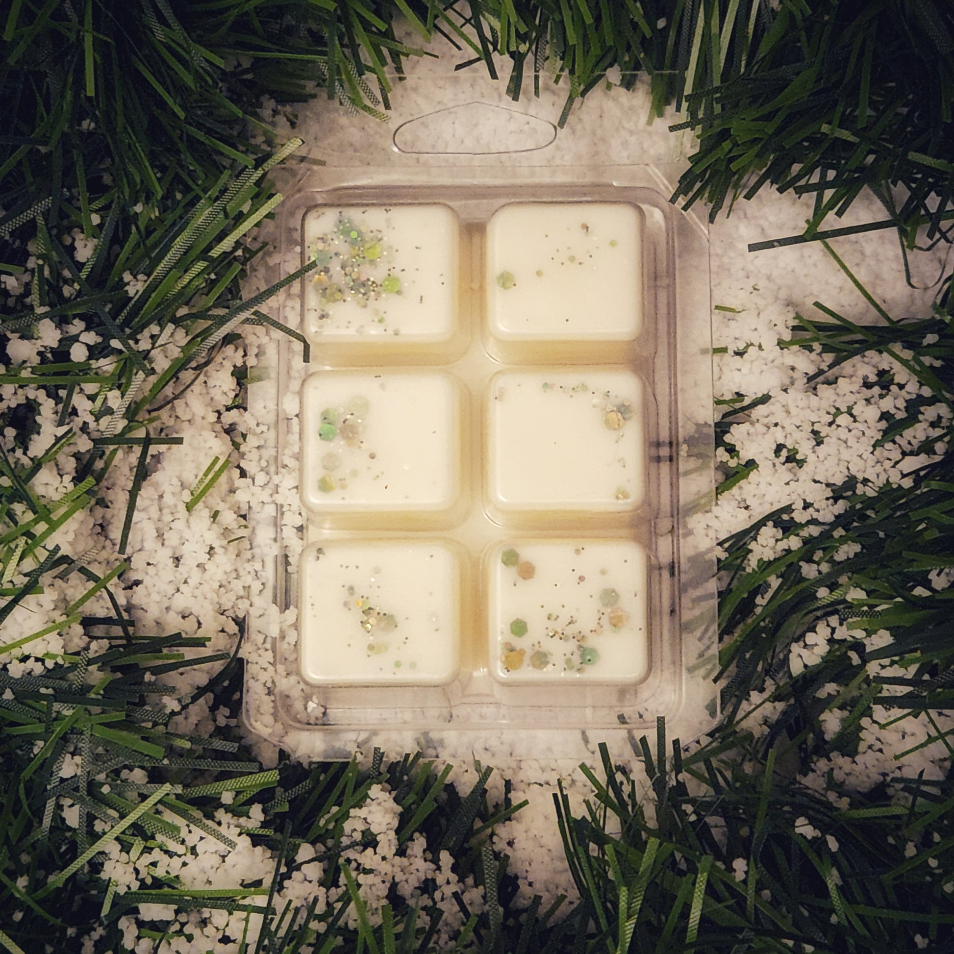 Packaged wax melts with decorative elements on a snowy grass background