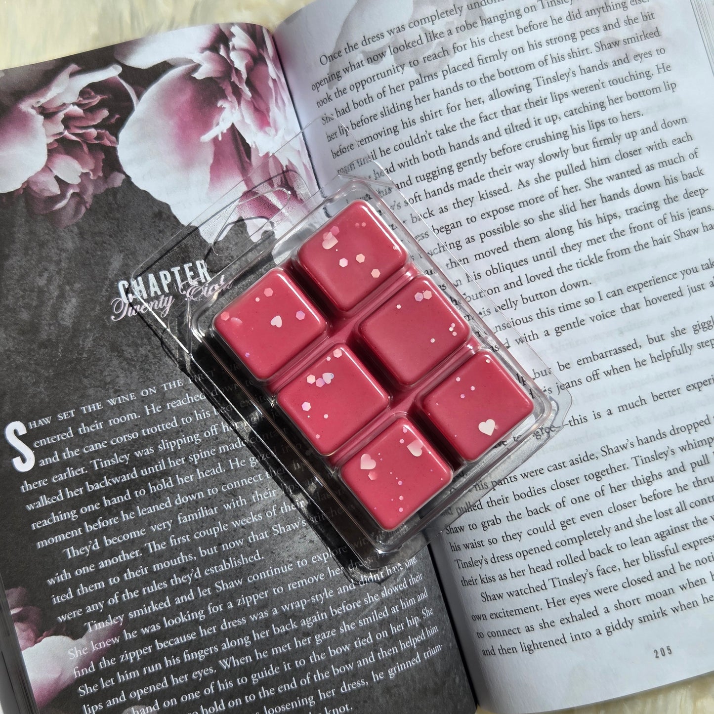 A set of six red wax melts in a clear plastic clamshell package placed on top of an open book with printed text.